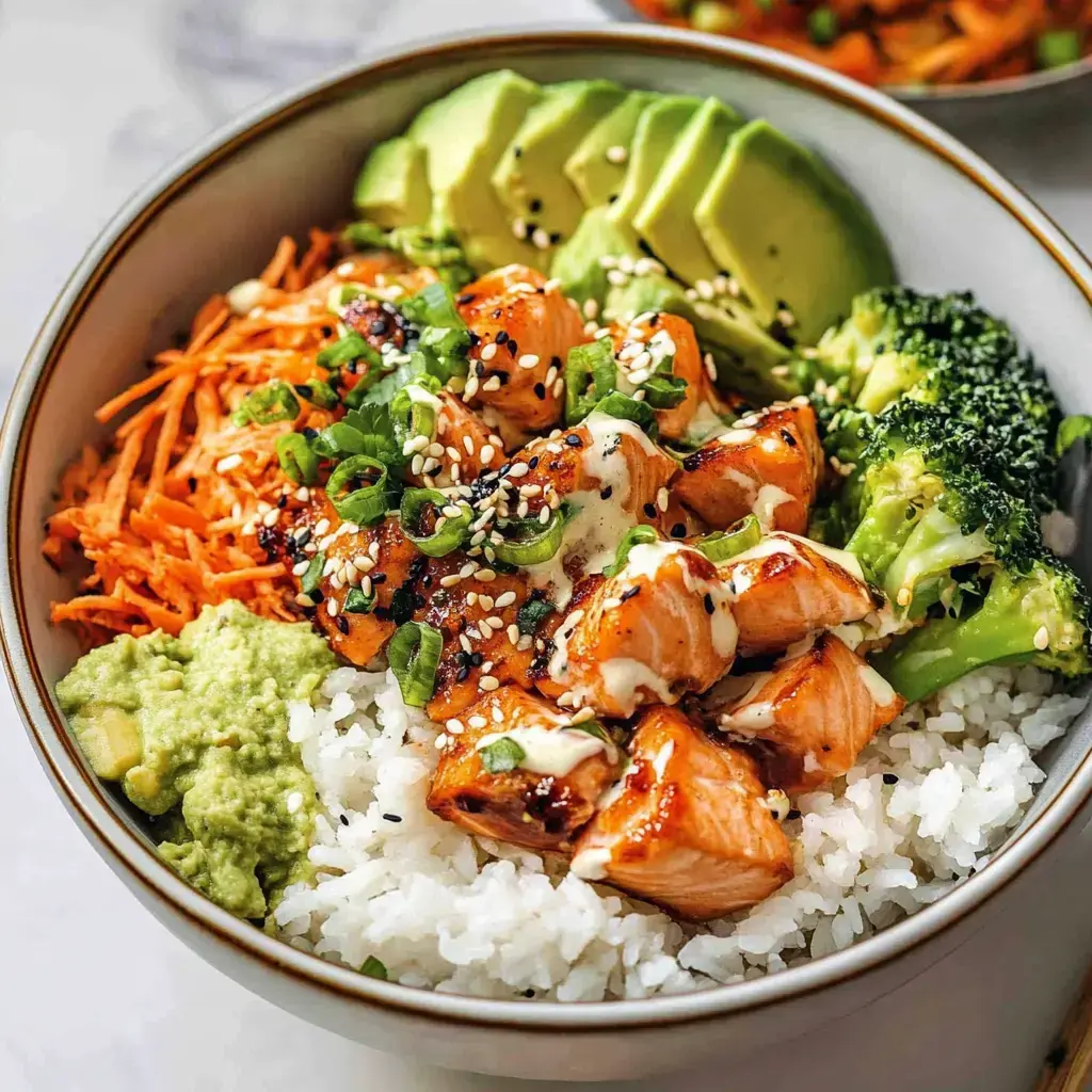 Eine Schüssel mit Reis, gebratenem Lachs, Karotten, Brokkoli, Avocado, Sesam und einer cremigen Sauce.