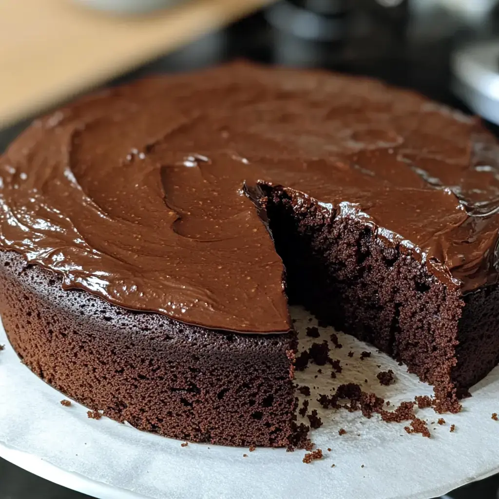 Saftiger Schokoladenkuchen mit glänzendem Schokoguss und herausgeschnittenem Stück.