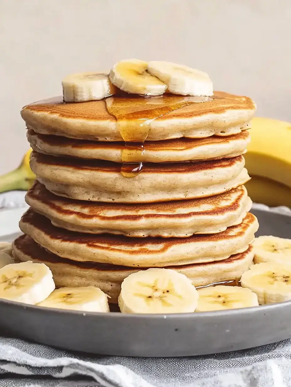 Ein Stapel goldener Pancakes mit Bananen und Honig auf einem Teller angerichtet.
