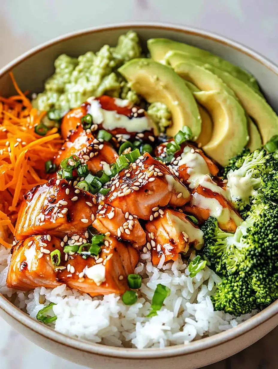 Eine Schüssel mit Reis, gegrilltem Lachs, Avocadoscheiben, Brokkoli, Karottenstreifen und einer cremigen Sauce, garniert mit Sesam und Frühlingszwiebeln.