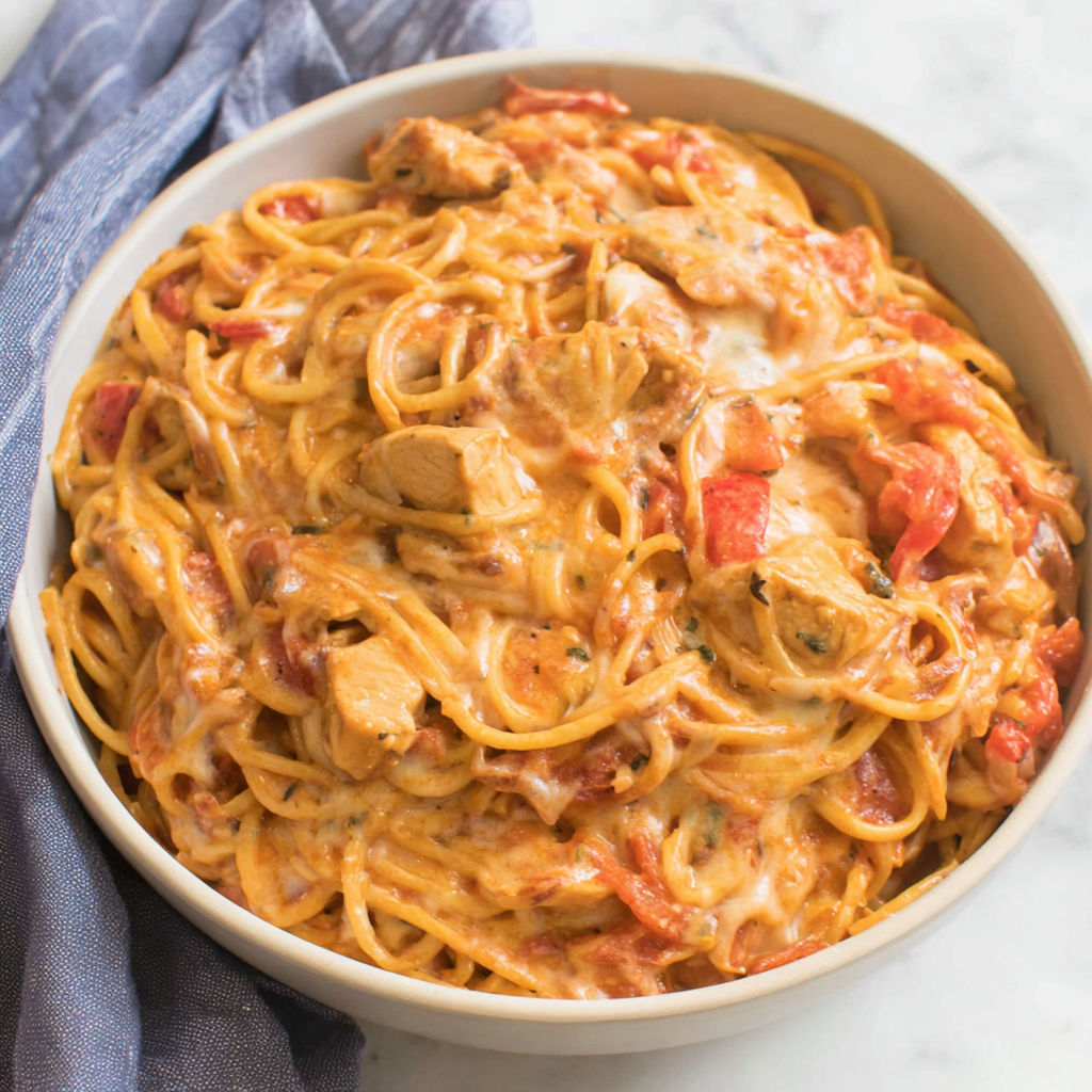 A bowl of spaghetti with chicken and tomatoes.