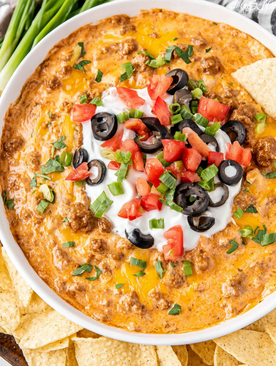 A bowl of chili with black olives and tomatoes.