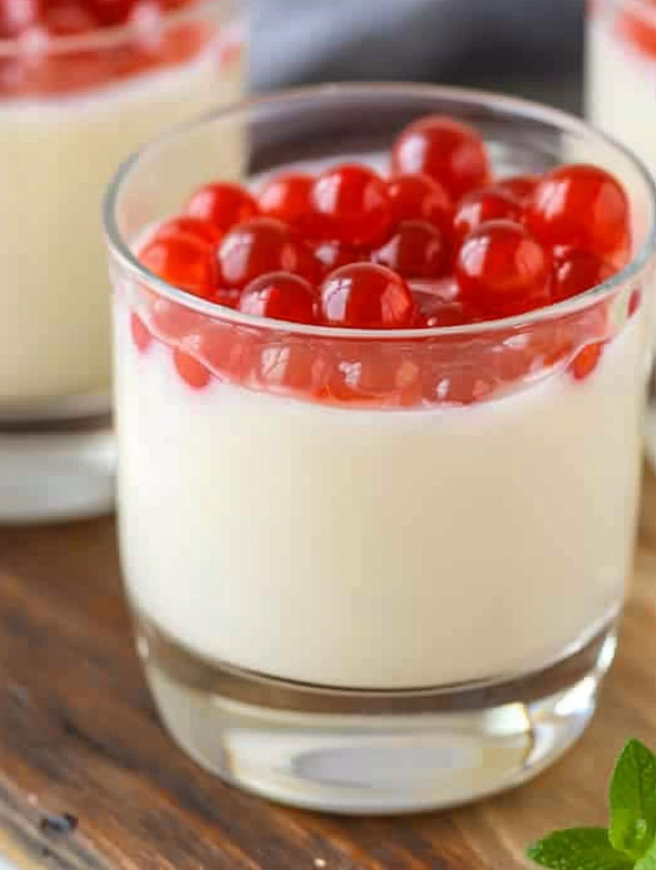 A glass of cream cheese panna cotta with red berries on top.