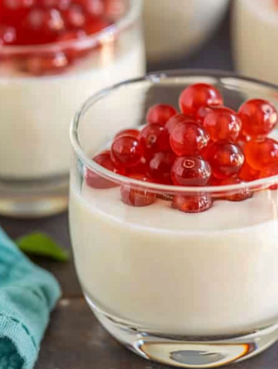A glass of cream cheese panna cotta with red berries on top.