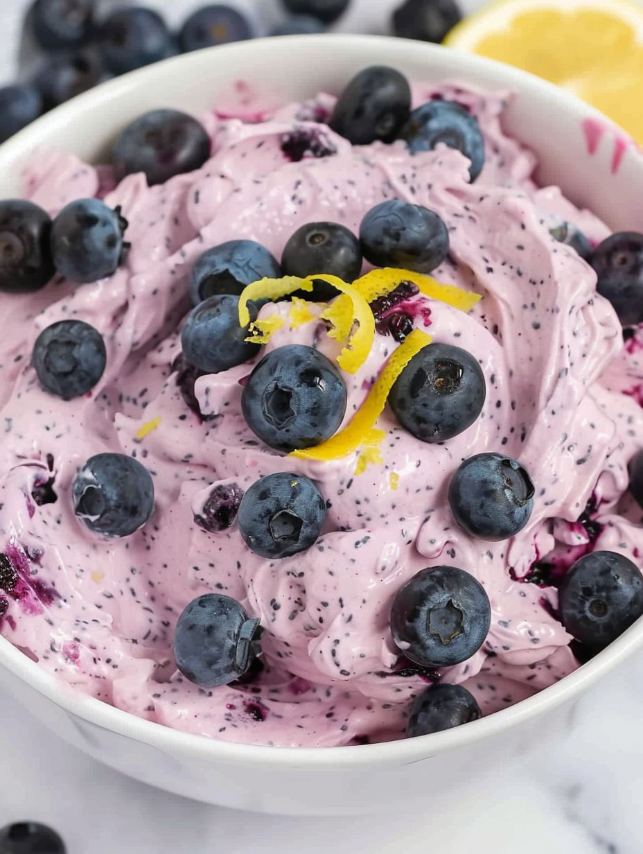 A bowl of blueberry fluff with a lemon wedge on top.