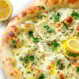 A slice of pizza with lemon and herbs on top.