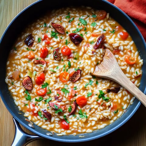 Im Topf liegt cremiger Reis mit Kirschtomaten und frischen Kräutern, angerichtet auf Holz.