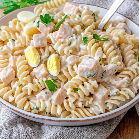 Auf einem Teller liegen Fusilli-Nudeln in cremiger Soße, dazu gebratene Hähnchenstücke, frische Petersilie und gekochte halbe Eier.