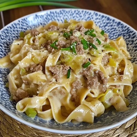 Bandnudeln in cremiger Sauce auf einem Teller, mit Hack, geschnittenem Lauch, Schnittlauch und Parmesan bestreut.