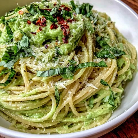 Ein weißer Teller mit einer cremigen Avocado Pasta, die mit Parmesan und Kräutern zubereitet wurde.