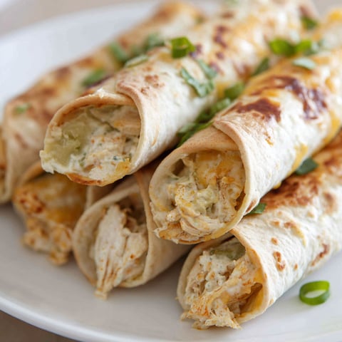 Baked creamy chicken taquitos on a white plate.