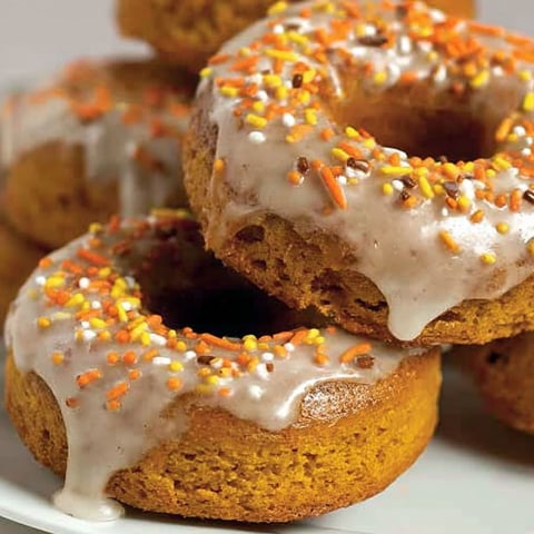 A plate of donuts with white frosting and orange sprinkles.