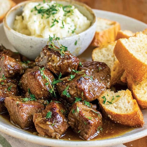 A plate of steak bites with garlic butter and herbs.