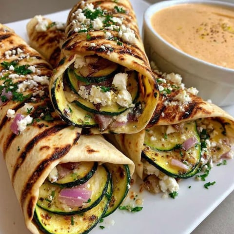 A plate of zucchini feta wraps with a side of zucchini dip.