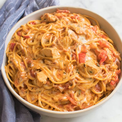 A bowl of spaghetti with chicken and tomatoes.