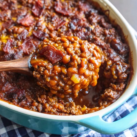 A wooden spoon is in a bowl of baked beans.