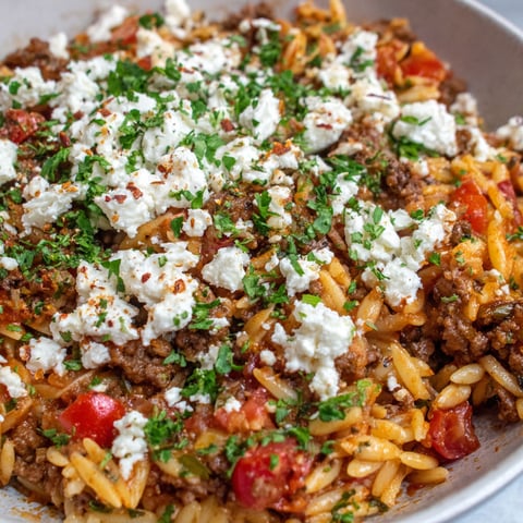 A bowl of food with tomatoes, feta cheese, and pasta.