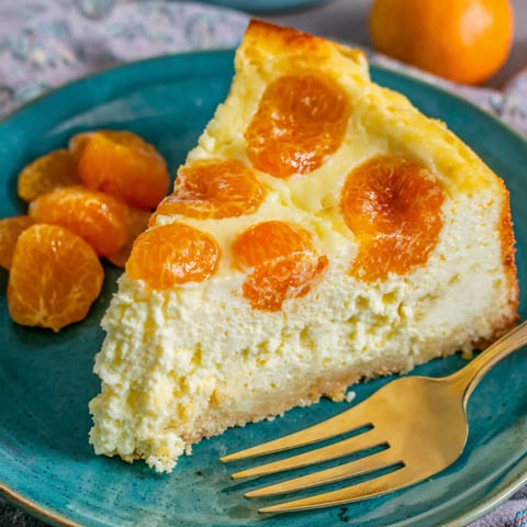 A slice of quark cheesecake with mandarin orange slices on a blue plate.