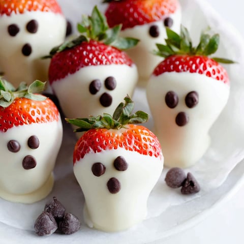 A plate of chocolate covered strawberries with white icing and chocolate eyes.