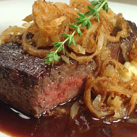 A close up of a steak with onions on top.