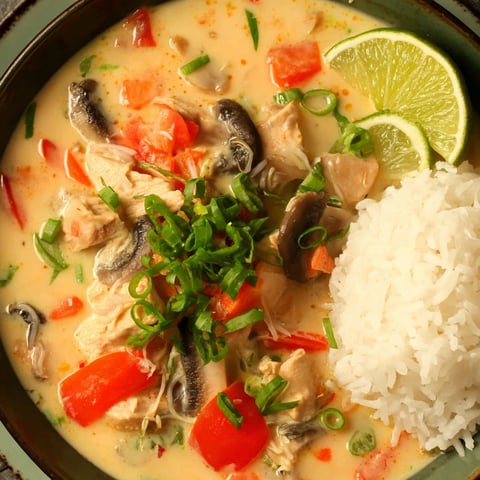 A bowl of Tom Kha Gai soup with rice and lime.