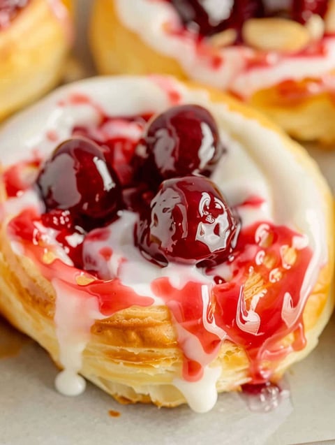 A close up of a cherry danish with white frosting.