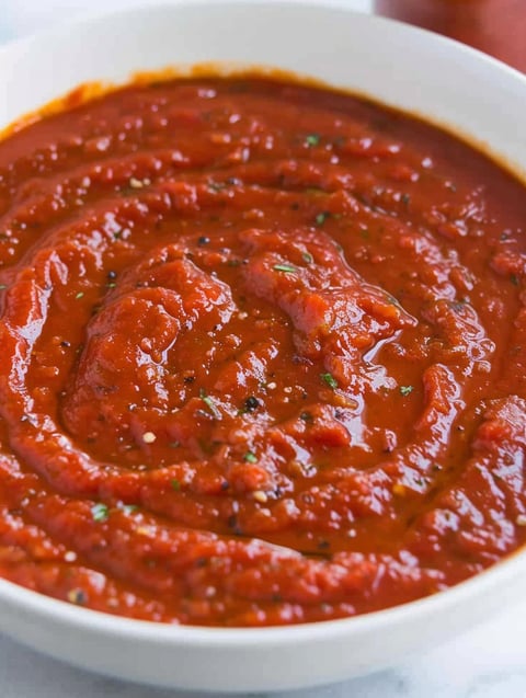 A bowl of red sauce with spices in it.