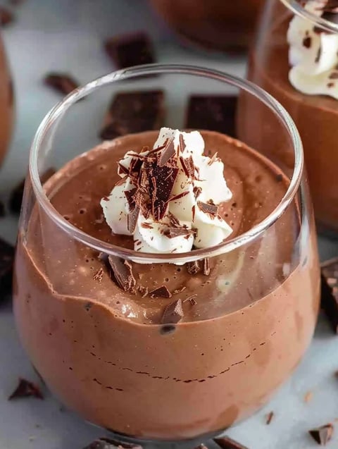 A glass of chocolate mousse with white whipped cream.