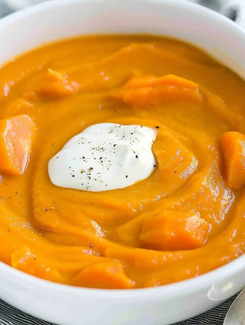A bowl of creamy potato carrot soup with a dollop of sour cream on top.