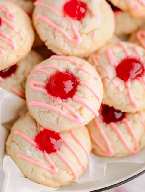 A plate of pink and white cookies with cherries on top.